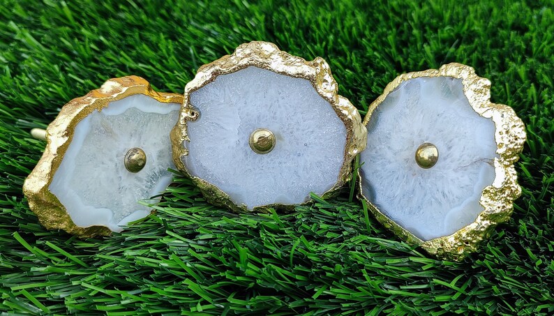 May include: Three white agate knobs with gold trim. The knobs have a round shape and a small gold knob in the center.