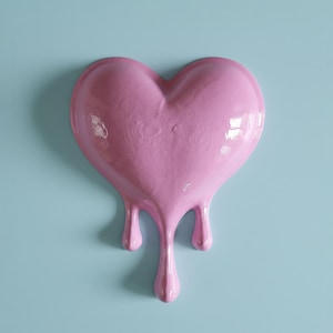 Puede incluir: Una escultura en forma de corazón rosa con efecto goteo. El corazón es de color rosa liso y brillante, y los goteos se extienden hacia abajo. El fondo es azul claro, proporcionando contraste con el corazón rosa.