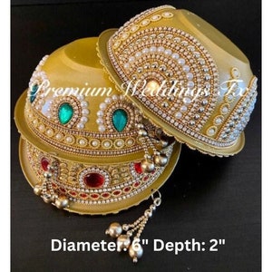 Può includere: Due ciotole dorate decorate con perle, strass e pietre preziose verdi e rosse. Le ciotole hanno un diametro di 15 cm e una profondità di 5 cm.