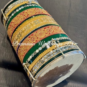 May include: A green and gold decorated drum with a white head. The drum is decorated with red, gold, and silver trim. The drum is a traditional Indian musical instrument.