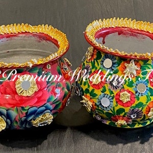 Può includere: Due ciotole di metallo decorative con motivi floreali. La ciotola a sinistra è rossa con fiori rosa e blu. La ciotola a destra è gialla con fiori multicolori. Entrambe le ciotole hanno un bordo dorato e piccoli specchi.