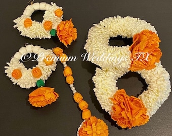 May include: A set of white flower garlands with orange flower accents. The set includes two smaller garlands, a larger garland, and a long garland with a pearl and orange bead strand.