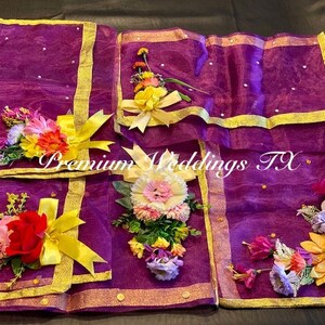 May include: Purple fabric squares with gold trim and floral embellishments. The fabric is sheer and has a subtle shimmer. The flowers are made of silk and are in shades of yellow, pink, and white. The text "Premium Weddings TX" is printed on the fabric.