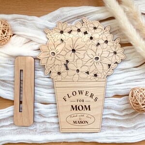 Op de afbeelding: Houten uitsnijding van een boeket bloemen in een pot met de tekst "Flowers for Mom" en "Picked with love by Mason".