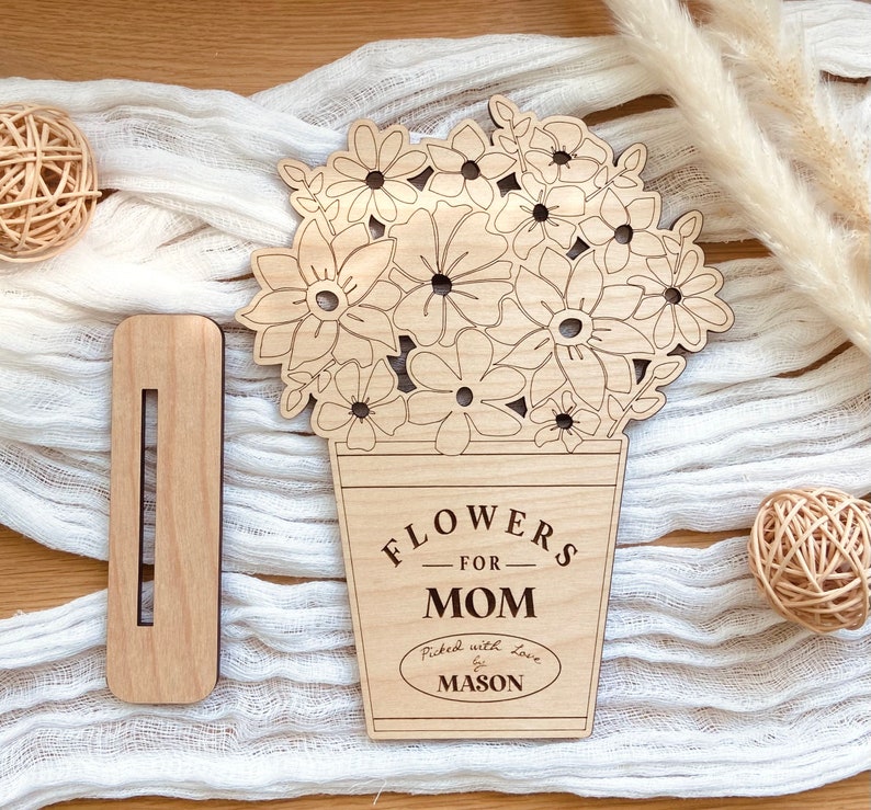 Op de afbeelding: Houten uitsnijding van een boeket bloemen in een pot met de tekst "Flowers for Mom" en "Picked with love by Mason".