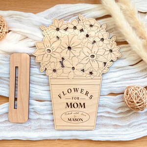 Op de afbeelding: Houten uitsnijding van een boeket bloemen in een pot met de tekst "Flowers for Mom" en "Picked with love by Mason".