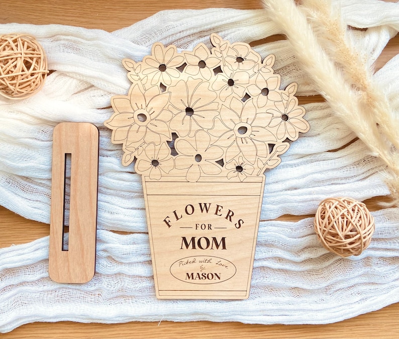 Op de afbeelding: Houten uitsnijding van een boeket bloemen in een pot met de tekst "Flowers for Mom" en "Picked with love by Mason".