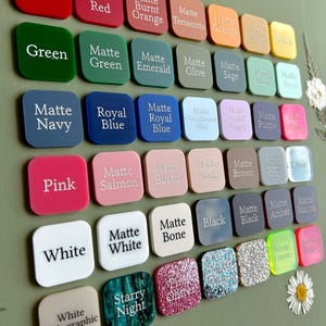 May include: A collection of square acrylic color swatches arranged in a grid, each labeled with its respective color name. The palette includes various shades of red, orange, yellow, green, blue, purple, pink, brown, gray, black, and white, featuring matte, glitter, and holographic finishes.
