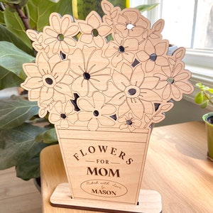 Op de afbeelding: Houten uitsnijding van een boeket bloemen in een vaas met de tekst "Flowers for Mom" en "Picked with love by Mason".