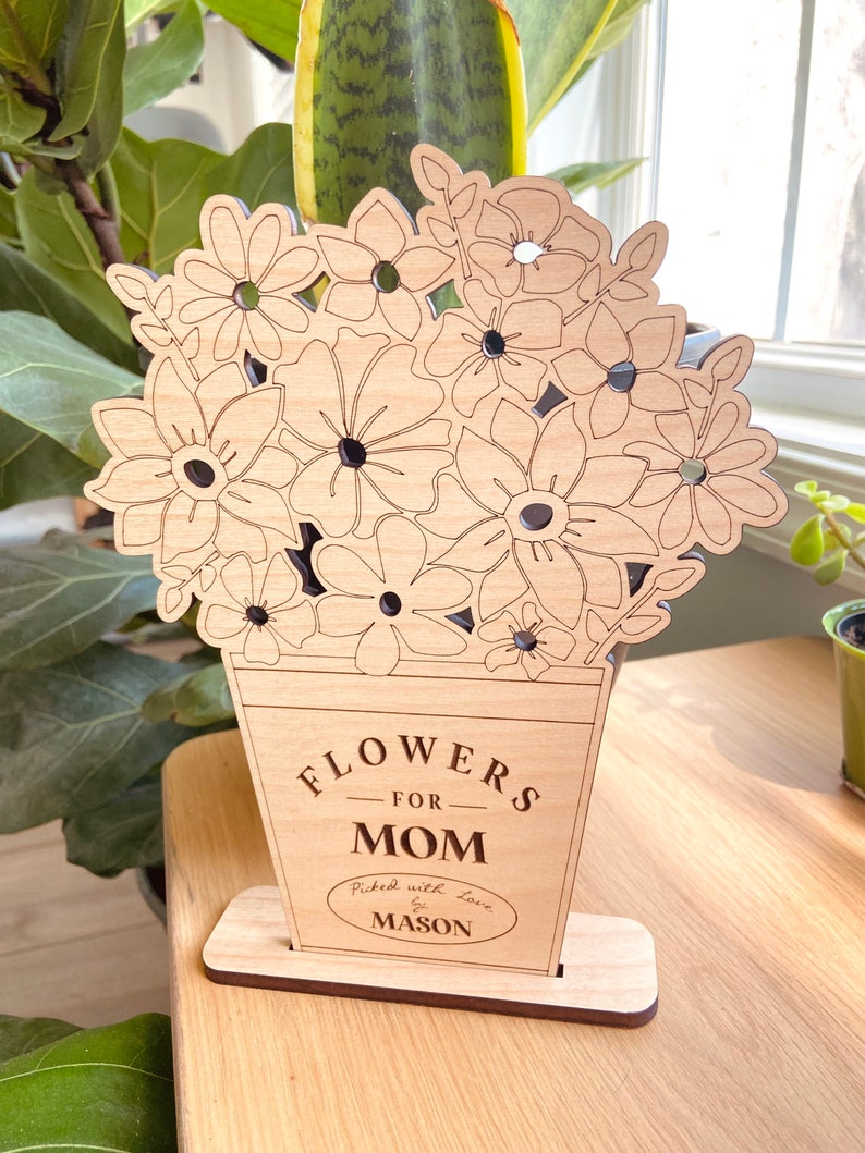 Op de afbeelding: Houten uitsnijding van een boeket bloemen in een vaas met de tekst "Flowers for Mom" en "Picked with love by Mason".