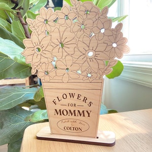 Op de afbeelding: Houten uitsnijding van een boeket bloemen in een vaas met de tekst "Flowers for Mommy Picked with love by Colton".