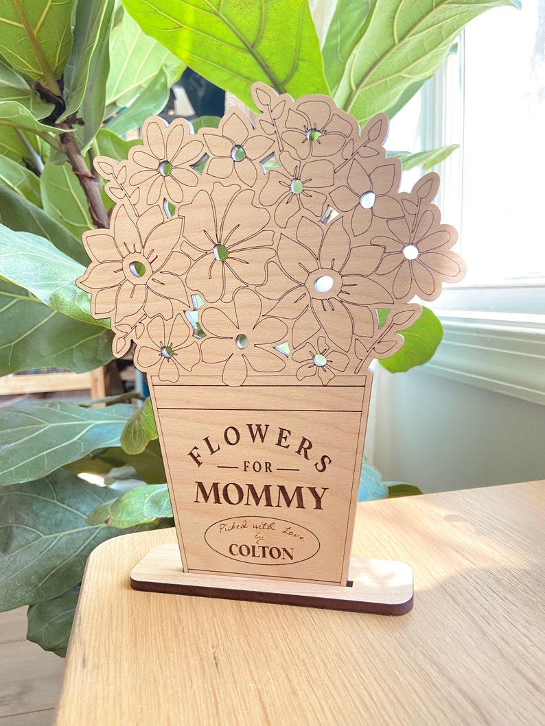 Op de afbeelding: Houten uitsnijding van een boeket bloemen in een vaas met de tekst "Flowers for Mommy Picked with love by Colton".