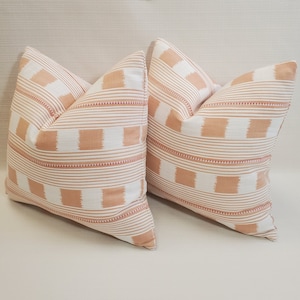 May include: Two peach and white striped throw pillows with a subtle pink and white checkered pattern. The pillows are on a white textured surface.