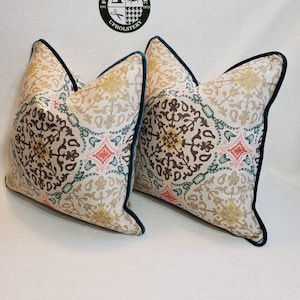 May include: Two decorative throw pillows with a beige background and a colorful geometric pattern. The pillows have a teal border.