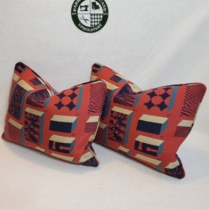 May include: Two red, blue, and beige patterned throw pillows with a geometric design. The pillows have a cream colored background with a geometric pattern in red, blue, and beige.