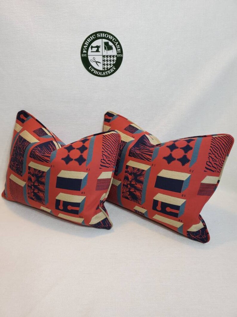 May include: Two red, blue, and beige patterned throw pillows with a geometric design. The pillows have a cream colored background with a geometric pattern in red, blue, and beige.