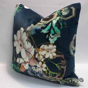 May include: A square decorative pillow with a dark blue background and a floral pattern. The flowers are white and pink with green stems and leaves. The pillow has a soft, velvety texture.