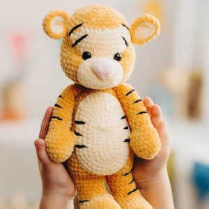 Peut inclure: Une peluche tigre faite à la main, aux tons orange, crème et noir. Le tigre a un ventre et un visage crème, avec des rayures et des détails noirs. Le jouet est doux et câlin, pour les enfants.