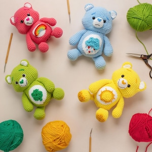 Peut inclure: Quatre ours en peluche au crochet faits à la main, roses, bleus, verts et jaunes. Chaque ours a un emblème unique sur le ventre et est entouré de fil, de crochets et de ciseaux. L'ours rose présente un arc-en-ciel, l'ours bleu un nuage, l'ours vert un trèfle et l'ours jaune un soleil.