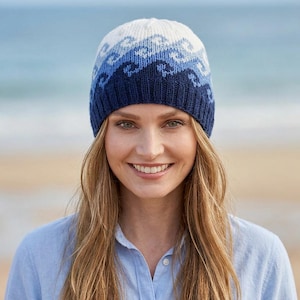 May include: A knit beanie featuring a gradient pattern of ocean waves in shades of white, light blue, medium blue, and dark navy blue. The hat has a ribbed cuff at the base and a rounded crown, showcasing a detailed jacquard knit design throughout.
