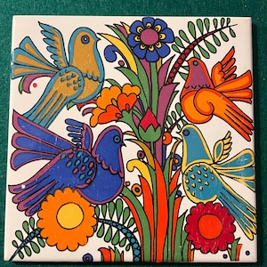 Może przedstawiać: Kwadratowa płytka ceramiczna z kolorową ilustracją ptaków i kwiatów. Ptaki są w odcieniach niebieskiego, pomarańczowego i żółtego, ze szczegółowymi wzorami skrzydeł. Kwiaty są pomarańczowe, czerwone i niebieskie, z zielonymi liśćmi. Tło jest białe.