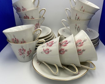 Pode incluir: Um conjunto de chávenas e pires vintage. As chávenas e pires de porcelana branca apresentam um design floral rosa e acabamentos dourados. As chávenas têm pegas curvas. O conjunto inclui várias chávenas e pires, empilhados ordenadamente.