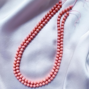 May include: Two strands of round, light pink beads strung on thin thread. The beads have a smooth, matte finish and are uniform in size, arranged in parallel lines to form a long, continuous loop of circular, light pink colored jewelry components.