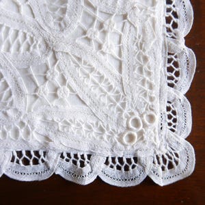 Peut inclure: Gros plan sur un napperon carré en dentelle blanche avec des motifs floraux et géométriques complexes. Les bords sont festonnés, ajoutant une touche délicate. La dentelle est faite d'un matériau fin et tissé.