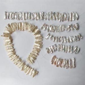 May include: A collection of white, elongated, irregular stick-shaped pearls arranged in one large circular strand and four smaller straight strands. Each pearl features a lustrous, textured surface with natural ridges and a distinct, uneven shape.