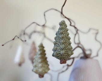 Puede incluir: Tres adornos de árbol de Navidad de ganchillo en tonos verdes y blancos colgados de una rama. Los adornos están decorados con purpurina y tienen un aspecto rústico y hecho a mano.