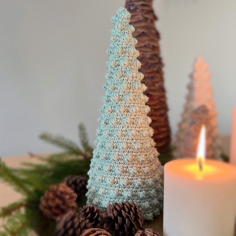 K&ouml;nnte beinhalten: Ein geh&auml;kelter hellblauer Weihnachtsbaumschmuck mit einer strukturierten Oberfl&auml;che. Der Schmuck liegt auf einem Tisch mit Kiefern&auml;sten und Tannenzapfen.