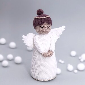 May include: A white crocheted angel with brown hair and a gold halo. The angel is wearing a white dress and has its hands clasped in front of it.
