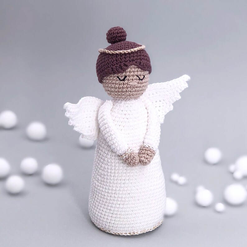 May include: A white crocheted angel with brown hair and a gold halo. The angel is wearing a white dress and has its hands clasped in front of it.