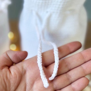 May include: White crocheted drawstring with two cords. The cords are braided and are tied together at the end.