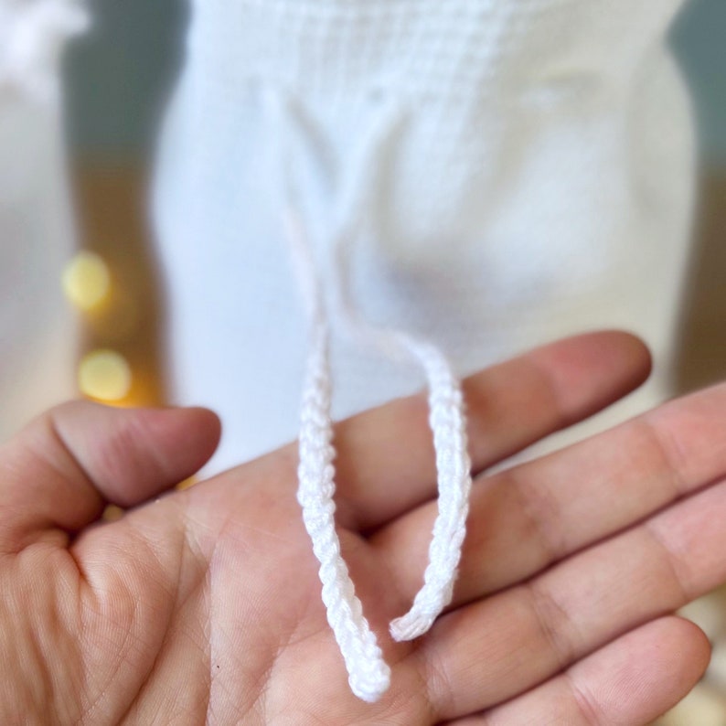May include: White crocheted drawstring with two cords. The cords are braided and are tied together at the end.