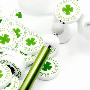 Peut inclure: Stylet vert et blanc avec un charme rond blanc qui dit "Blessed. Loved. Lucky." avec un tr&egrave;fle &agrave; quatre feuilles vert au centre. Le charme est attach&eacute; &agrave; une perle grise et une perle blanche.