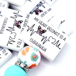 May include: White rectangular charms with the text "MY HEART BELONGS TO A CHIHUAHUA" and a Chihuahua graphic. A turquoise and floral bead keychain is in the foreground. The charms have a heartbeat design.