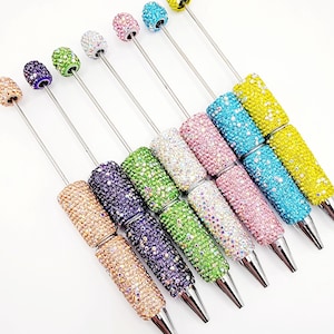 May include: Set of eight rhinestone pens in various colors, including pink, blue, green, and purple. Each pen has a silver metal body and a clear rhinestone tip.