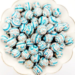 May include: A bowl filled with white, blue, and orange patterned round beads. The beads have a geometric design.