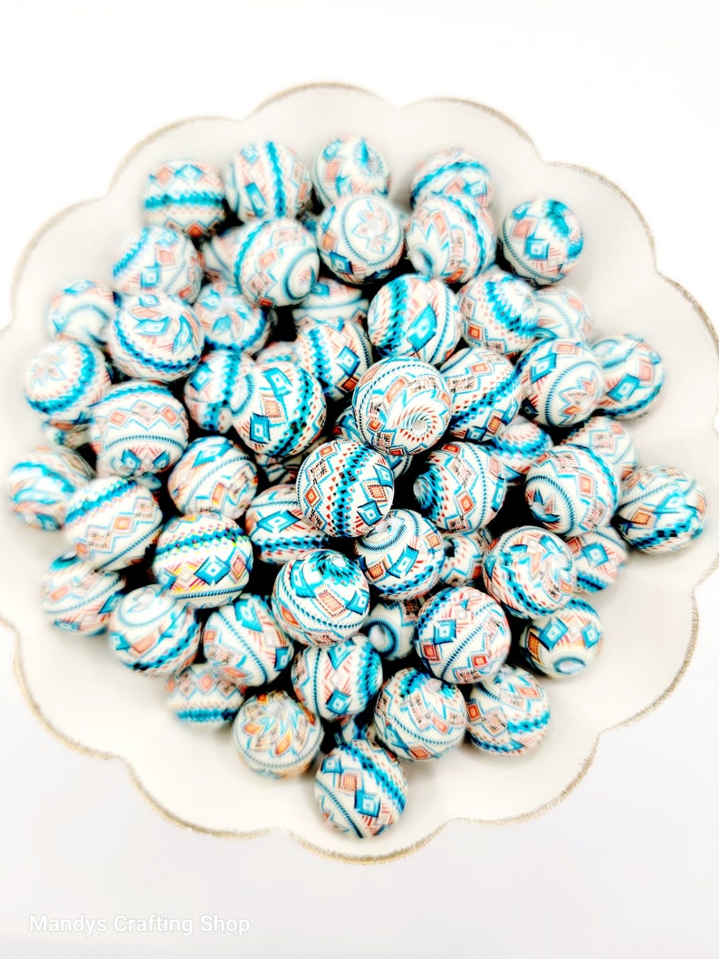 May include: A bowl filled with white, blue, and orange patterned round beads. The beads have a geometric design.