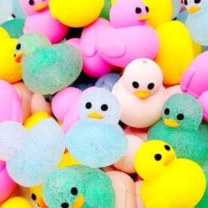May include: A collection of colorful rubber duck toys in various poses, including sitting, standing, and swimming. Some ducks have glitter accents. The ducks are in shades of yellow, pink, blue, and green.