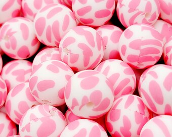 May include: A close-up of a pile of pink and white silicone beads with a cow print pattern. The beads are round and have a hole in the center.