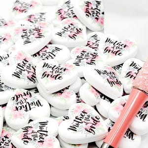 Może przedstawiać: Duża sterta białych serduszek z r&oacute;żowymi kwiatowymi wzorami i napisem "Matka Panny Młodej" czarnym pismem.