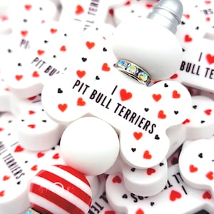 May include: White and red striped pen with a silver base and a decorative band of iridescent rhinestones. The pen is surrounded by white dog bone-shaped charms with the text "I PIT BULL TERRIERS" and red and black hearts.