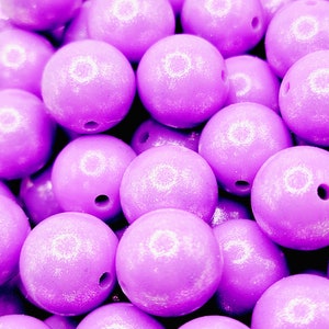 May include: Close-up of a pile of light purple, round beads. Each bead has a hole drilled through the center. The beads are smooth and have a glossy finish. The beads are for crafting.