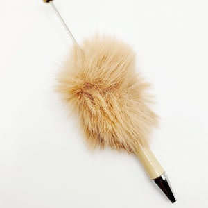 May include: A brown faux fur pen with a silver tip and a beige cap. The pen is on a white background.