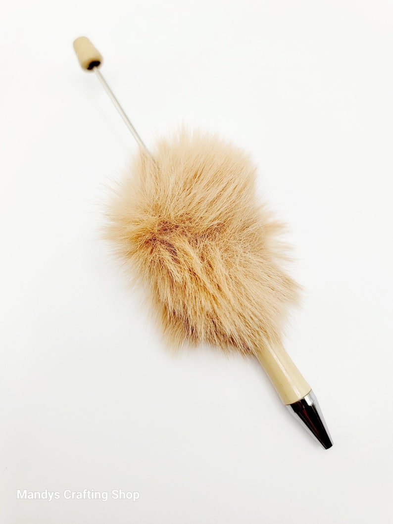 May include: A brown faux fur pen with a silver tip and a beige cap. The pen is on a white background.