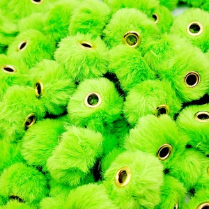 May include: A pile of bright green fuzzy pom poms with gold metal eyelets. The pom poms are all the same size and are arranged in a random pattern.