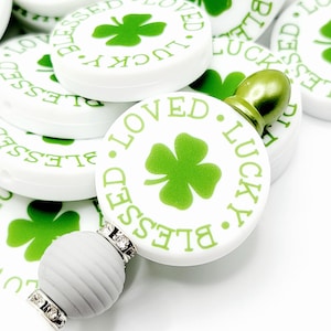 Peut inclure: Des bouchons de bouteille ronds blancs et verts avec le texte "Blessed Lucky Loved" et un tr&egrave;fle &agrave; quatre feuilles. Les bouchons de bouteille sont empil&eacute;s les uns sur les autres.