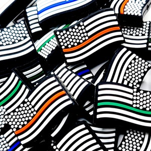 May include: A close-up of a pile of black and white American flag-themed rubber charms. The flags have a thin red, blue, or green stripe across them.